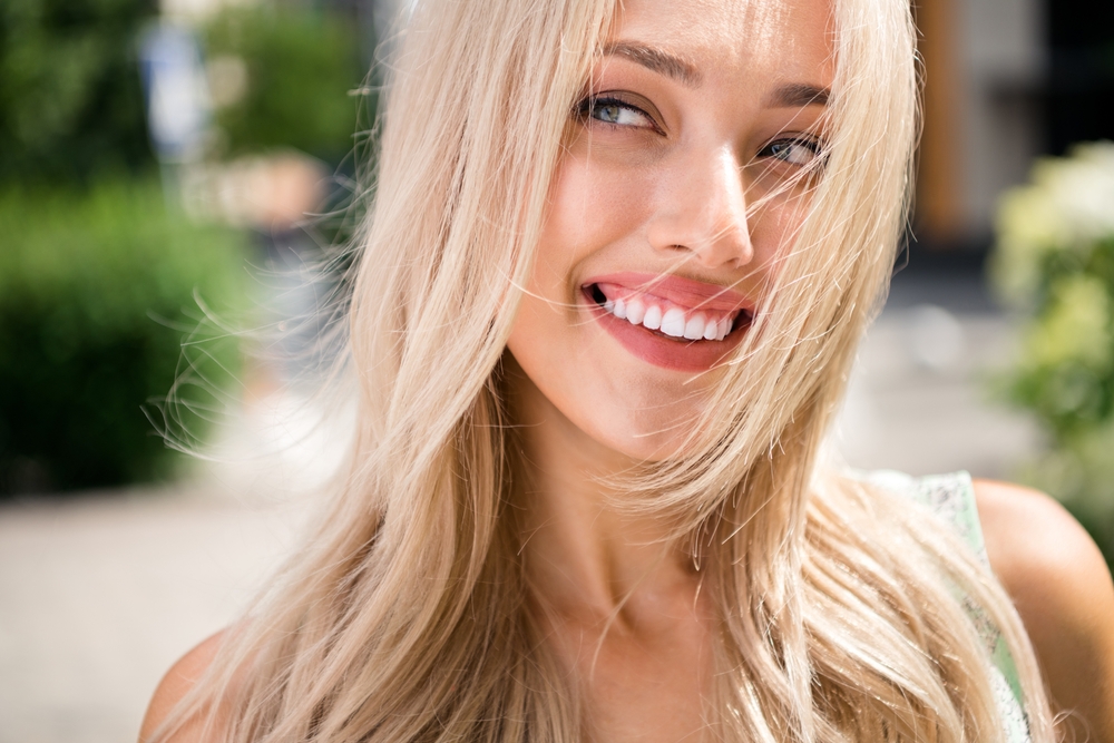 Gorgeous Smile Outdoors - Bellevue Cosmetic Dentistry A blonde woman smiling radiantly outdoors with perfect white teeth and wind-swept hair, symbolizing confidence after cosmetic dental care - Bellevue Cosmetic Dentistry
