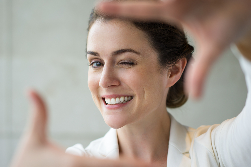 Winking Woman with Bright Smile - Dental Crowns Bellevue A cheerful woman winking and framing her face with her hands, confidently showing her perfect white teeth—results of restorative crown work - Dental Crowns Bellevue
