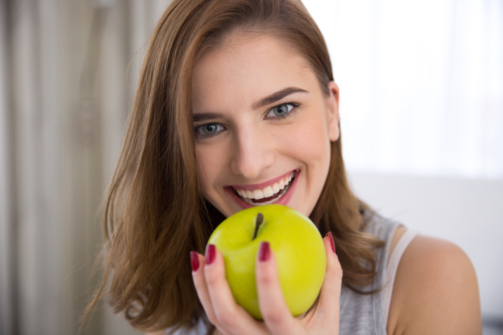 Closeup portrait of a happy young woman biting green apple - Dentures Bellevue WA Closeup portrait of a happy young woman biting green apple - Dentures Bellevue WA