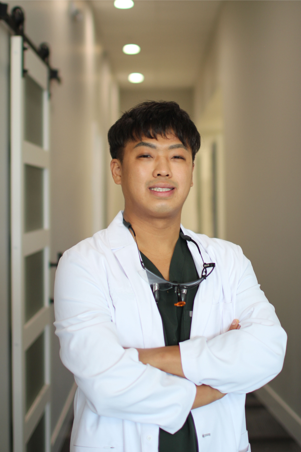 Dr. Sarah Park, DDS in a white coat stands in a clean, bright office environment with decorative greenery in the background - Newport Dental Bellevue WA