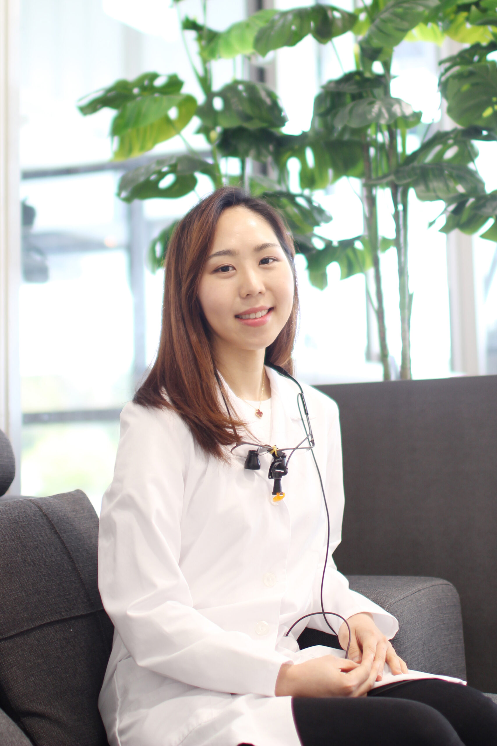 Dr. Alex Shin, DMD in a white coat, wearing dental loupes around his neck, smiles with arms crossed against a plain white background - Newport Dental Bellevue WA