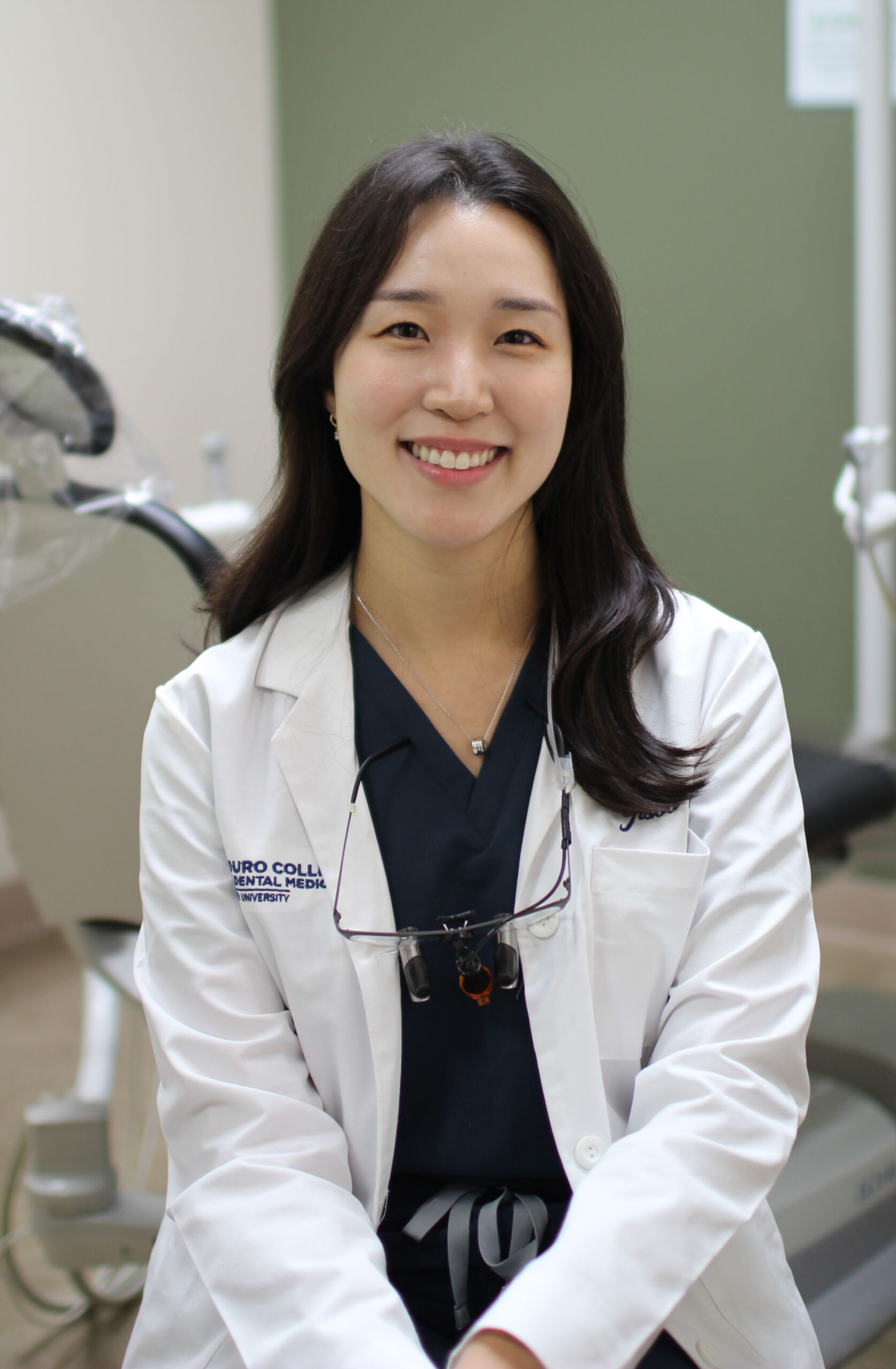 Dr. Brian Han, DMD in a white coat and glasses smiles confidently while leaning on a counter in a modern, professional office with minimalist decor - Newport Dental Bellevue WA