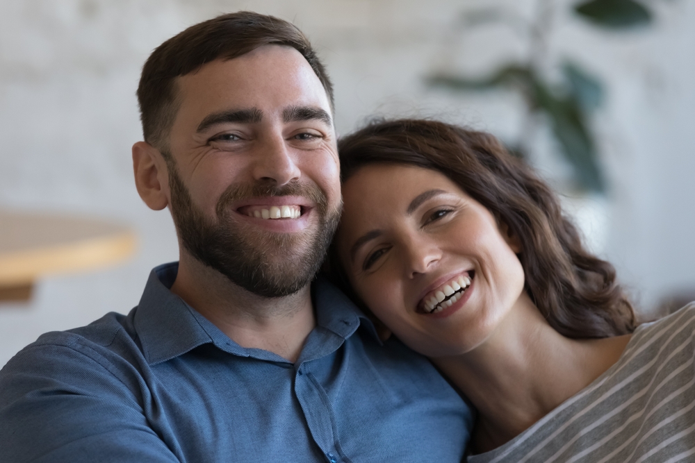 Happy Couple Smiling Together Indoors - Newport Dental Bellevue WA A cheerful couple sitting close together and smiling, showing healthy teeth and emotional connection—representing patient satisfaction - Newport Dental Bellevue WA