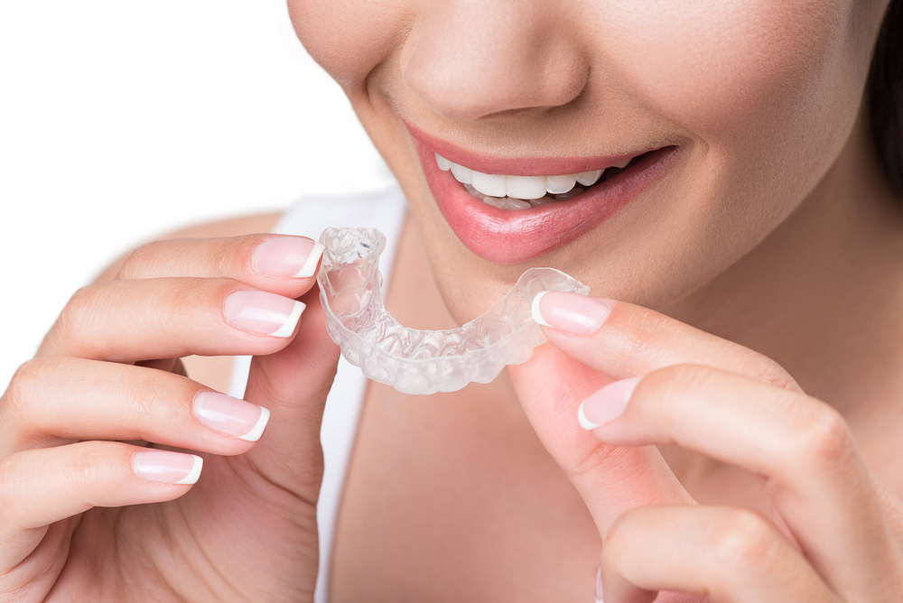 A woman with a bright smile and manicured nails holding a clear Invisalign aligner, highlighting aesthetic and comfortable orthodontic treatment - Invisalign Bellevue