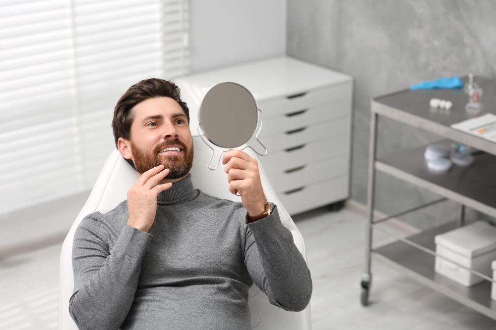 Natural-Looking Dental Crowns for Restored Smiles Man examining his new dental crowns in a mirror at a dental clinic