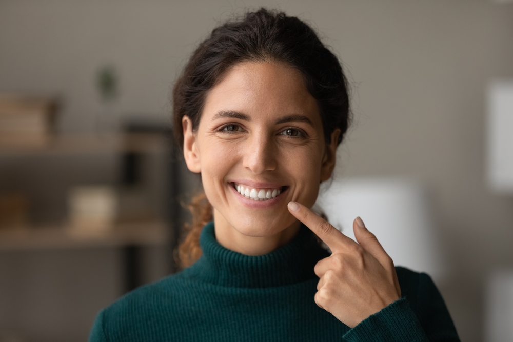 Bright Smile from Cleaning and Exams Smiling woman pointing to her clean teeth after a dental cleaning and exam