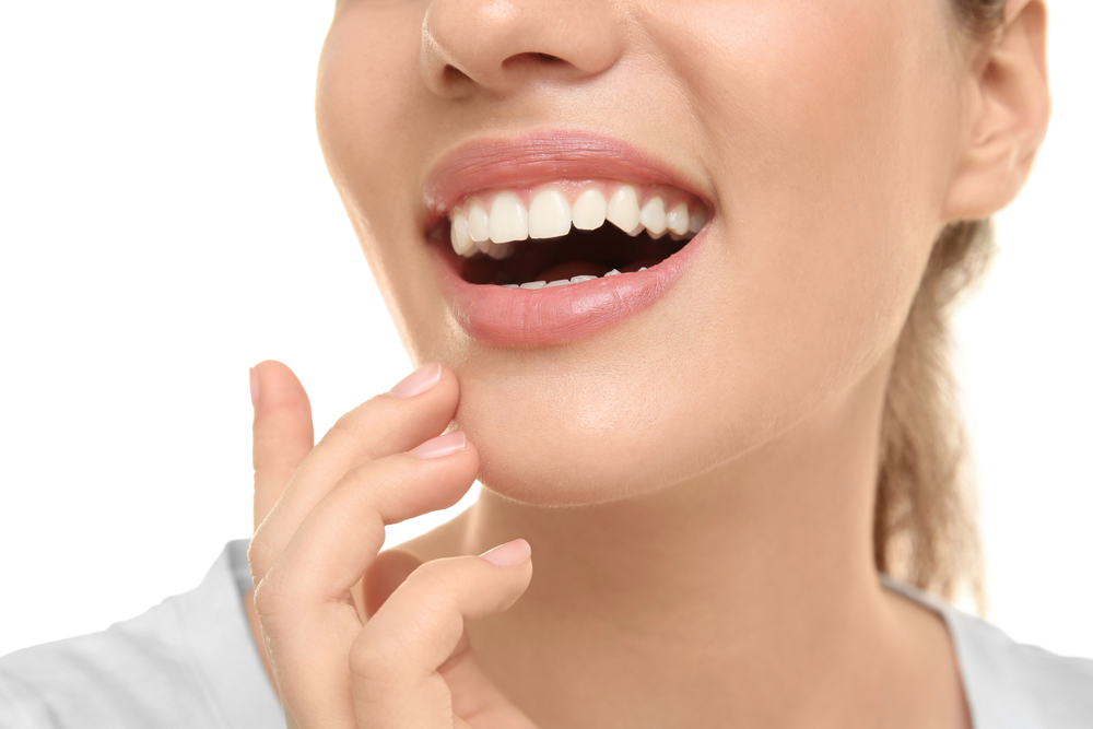 Perfect White Smile Close-Up - Dental Crowns Bellevue Close-up of a woman's bright, healthy teeth and soft pink lips as she gently touches her chin, illustrating natural-looking results of crown restoration - Dental Crowns Bellevue