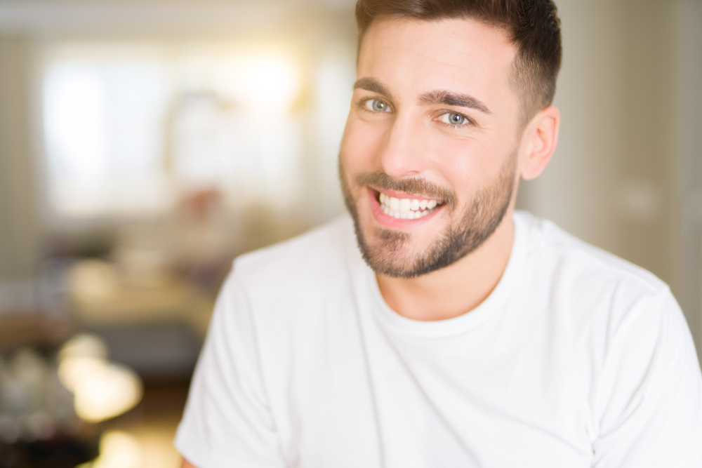 Bright White Smile Indoors - Teeth Whitening Bellevue A cheerful man in a white shirt smiles confidently indoors, showcasing the vibrant results of professional teeth whitening - Teeth Whitening Bellevue