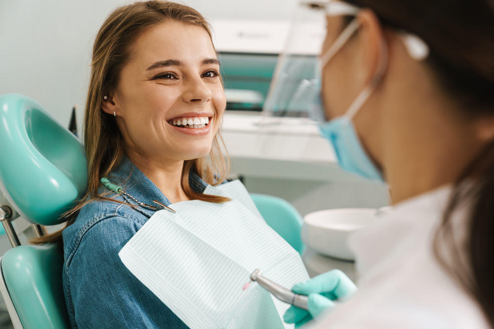 Smiling Patient at Dental Office - Experiencing an Emergency? Female patient smiling in dental chair during consultation with dentist - Experiencing an Emergency?